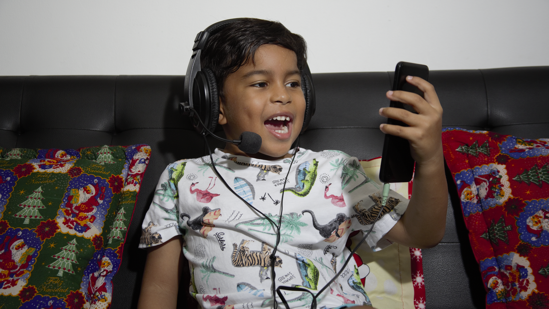 Fotografía: Niño sentado en un sofá usa audífonos de tipo diadema y habla frente a un celular